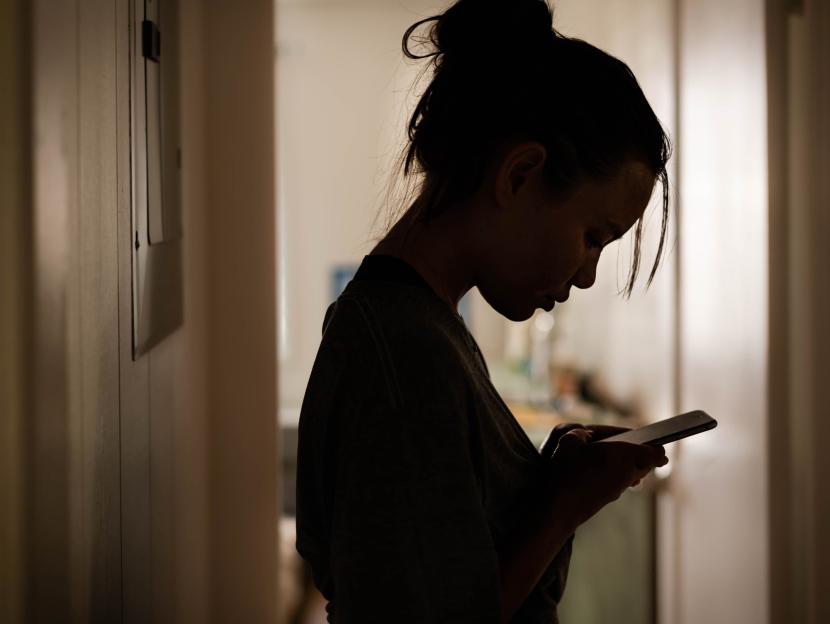 Silhouette of a gloomy woman looking at her phone.