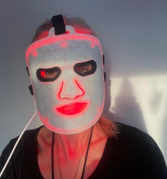 Woman wearing a white LED "Beaute Mask" emitting a red light.