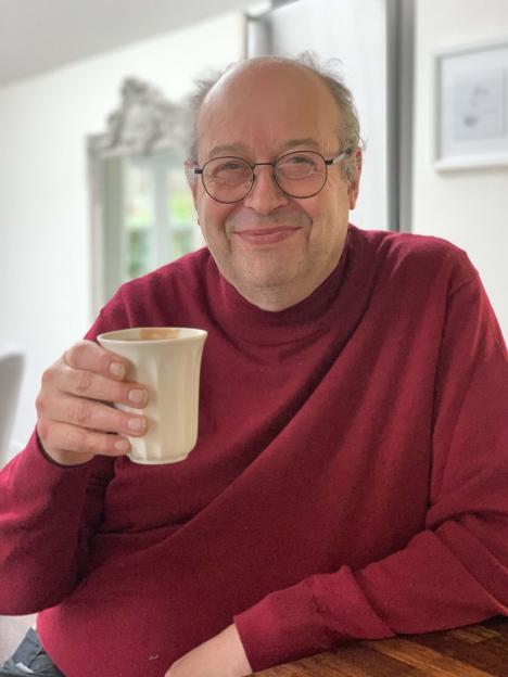 Rob Grant, a smiling English comedy writer, in a red turtleneck, holding a coffee cup.