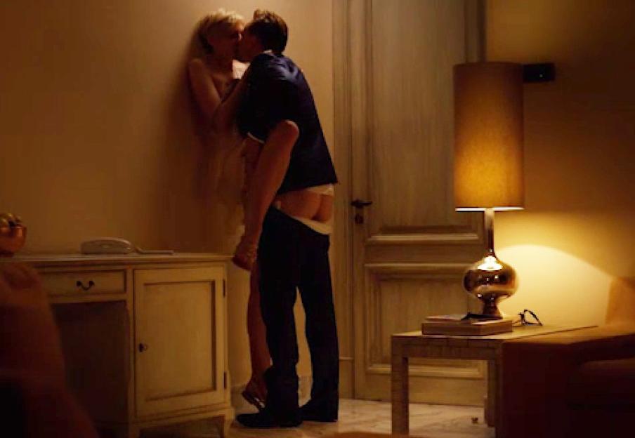 A couple kissing against a wall, with the man's pants down.