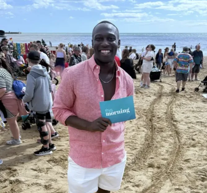 A man on a beach holds a blue card that says "this morning."