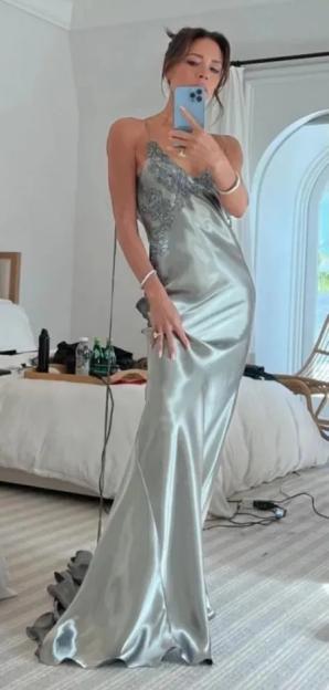 Victoria Beckham in a flowing silver gown with lace detailing, taking a mirror selfie.