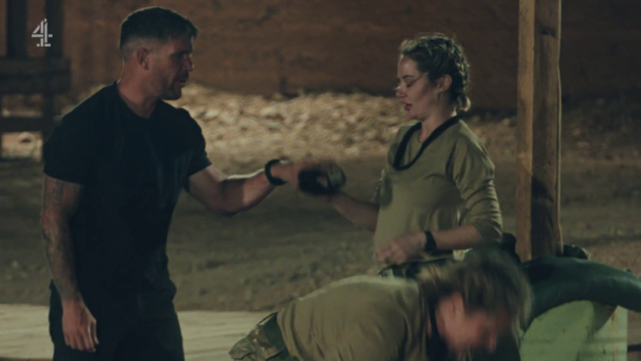 A man and a woman in military-style clothing engaging in a hand-to-hand combat exercise.