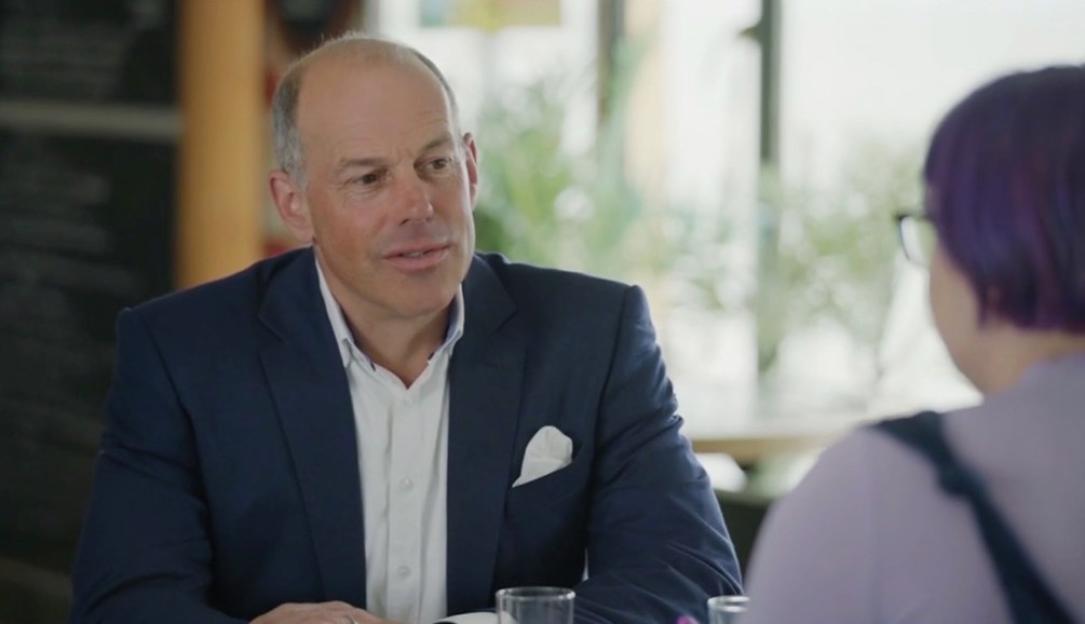 A man in a suit jacket looks toward a person with purple hair.