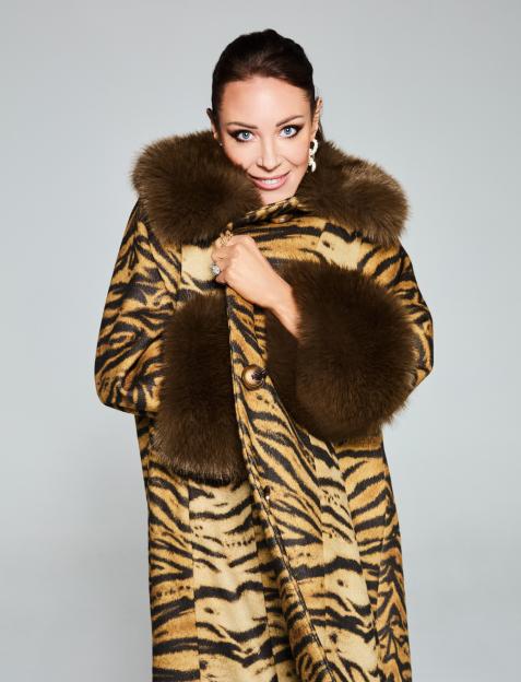 A smiling woman wearing a tiger print coat with fur trim.