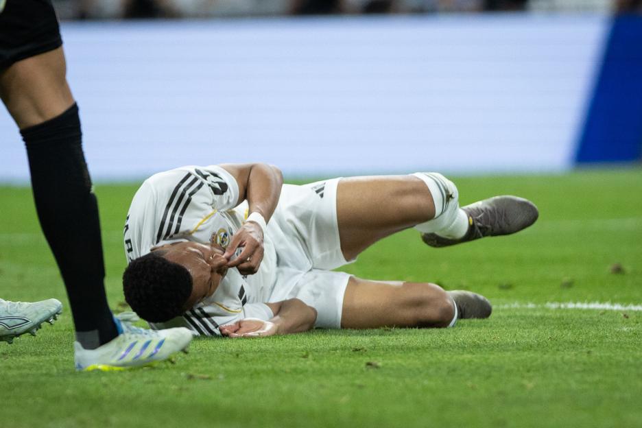 A Real Madrid CF player lying on the grass and holding his face during a match against Girona.