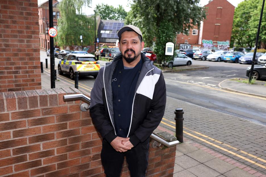 Mohammad Razor standing on a sidewalk near where an incident took place, with a police car in the background.