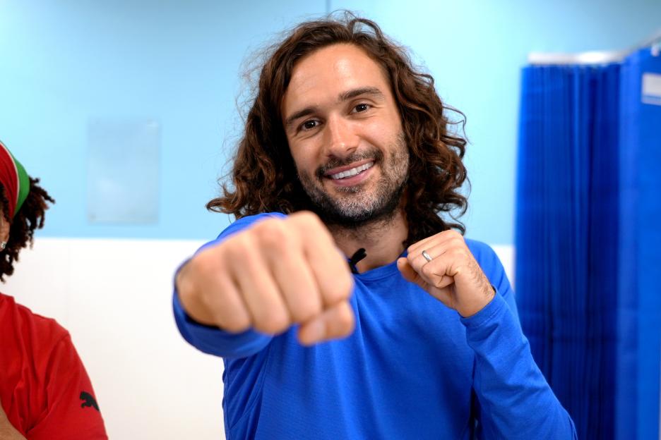 Joe Wicks smiling and posing with his fists up, ready to exercise.