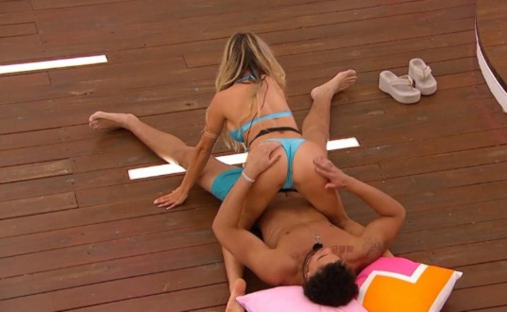A woman in a blue bikini straddling a man lying on a wooden deck.
