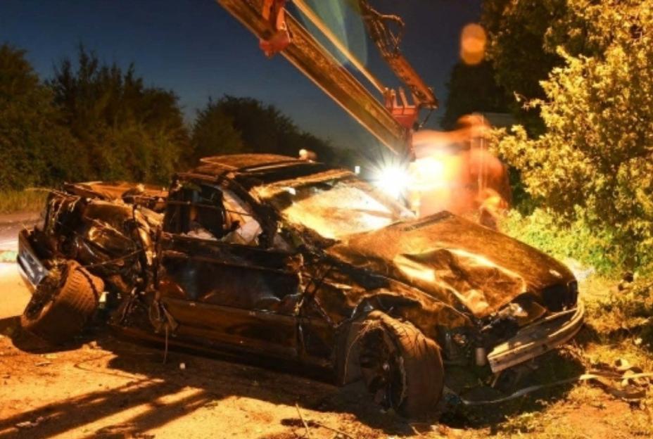 A severely damaged car being recovered by a crane after an accident.