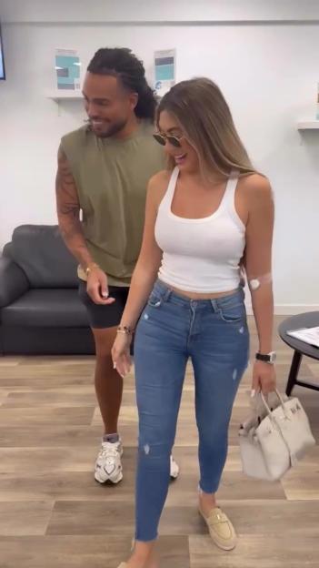 Two people walking, one woman wearing a white tank top and jeans with a glucose monitor on her arm, and a man with dreadlocks wearing a t-shirt and shorts.