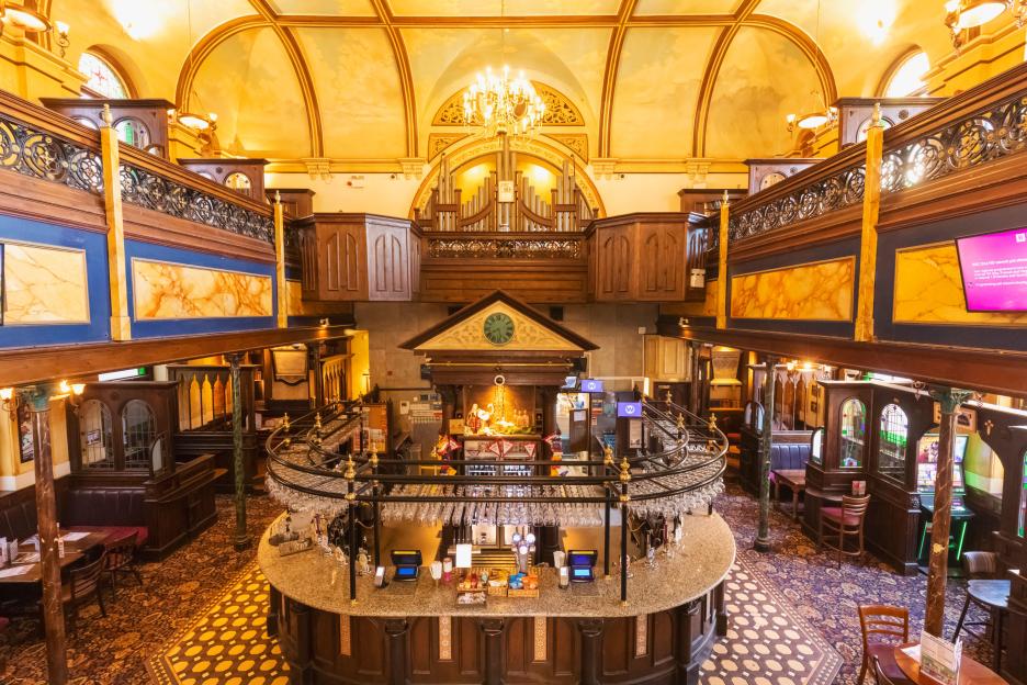 The interior of the Samuel Peto Wetherspoon pub in Folkestone, a converted chapel with a large central bar, ornate balconies, and a grand organ.