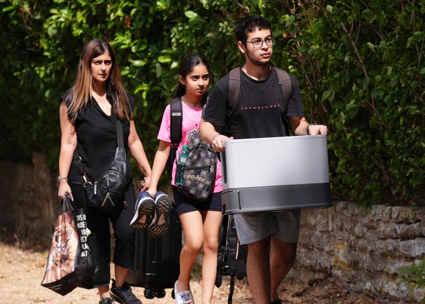 Three residents, a woman, a girl, and a young man, carry belongings as they evacuate their homes following a blaze.