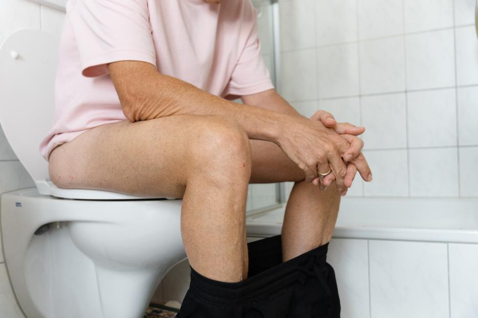 Mature man sitting on toilet while having stomach pain