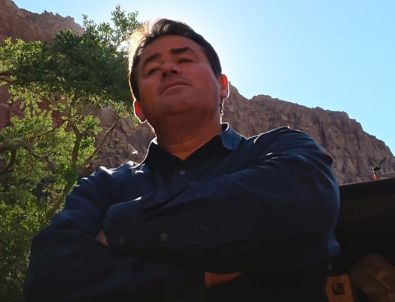 Samuel Bateman in a dark shirt with his arms crossed, looking up towards the camera.
