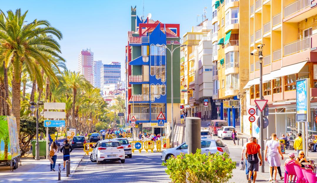 View of Benidorm, Spain, with palm trees, multi-colored buildings, and people walking along a street.