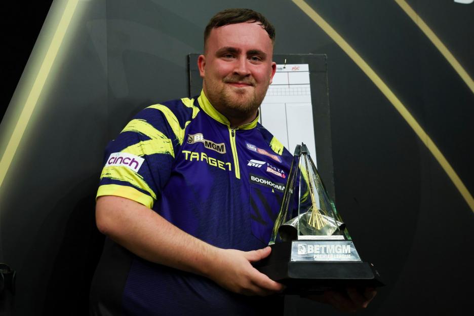 A man in a purple and yellow darts shirt holding the BetMGM Premier League darts trophy.