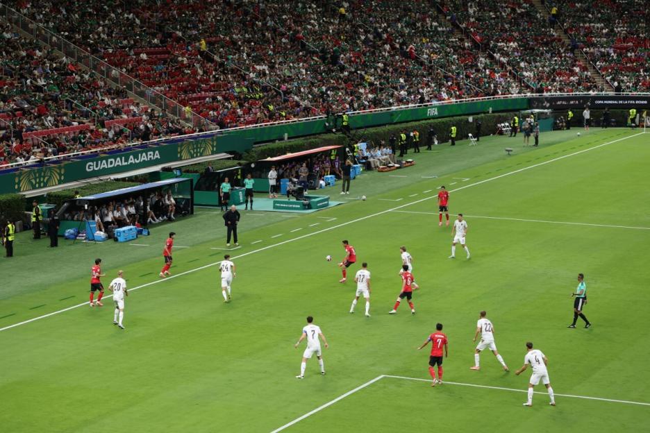 A wide shot of a soccer game between Korea Republic (red jerseys) and Czechia (white jerseys) at the FIFA World Cup 2026, with a large crowd in the stands.