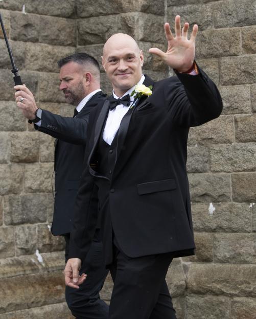 Tyson Fury in a black tuxedo waves at his wedding.