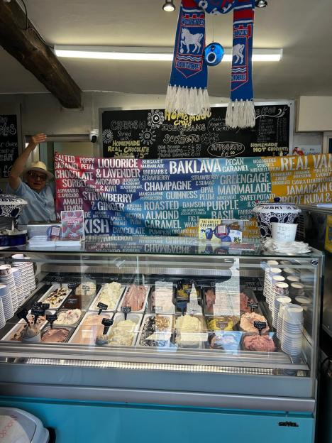 A man behind a glass display of unique ice cream flavors like lobster, black garlic, peach, and jalapeno.