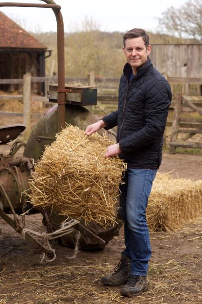 Matt Baker holding hay next to a tractor.