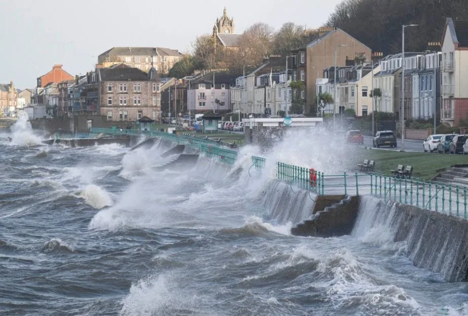Rough sea waves crashing violently against the coastal seawall and footpath in Inverclyde, Scotland, during a storm.