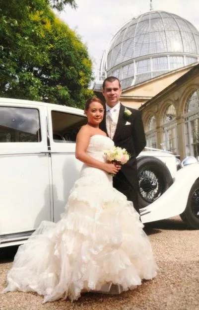Bride and groom in front of a white vintage car and a large glass dome building.