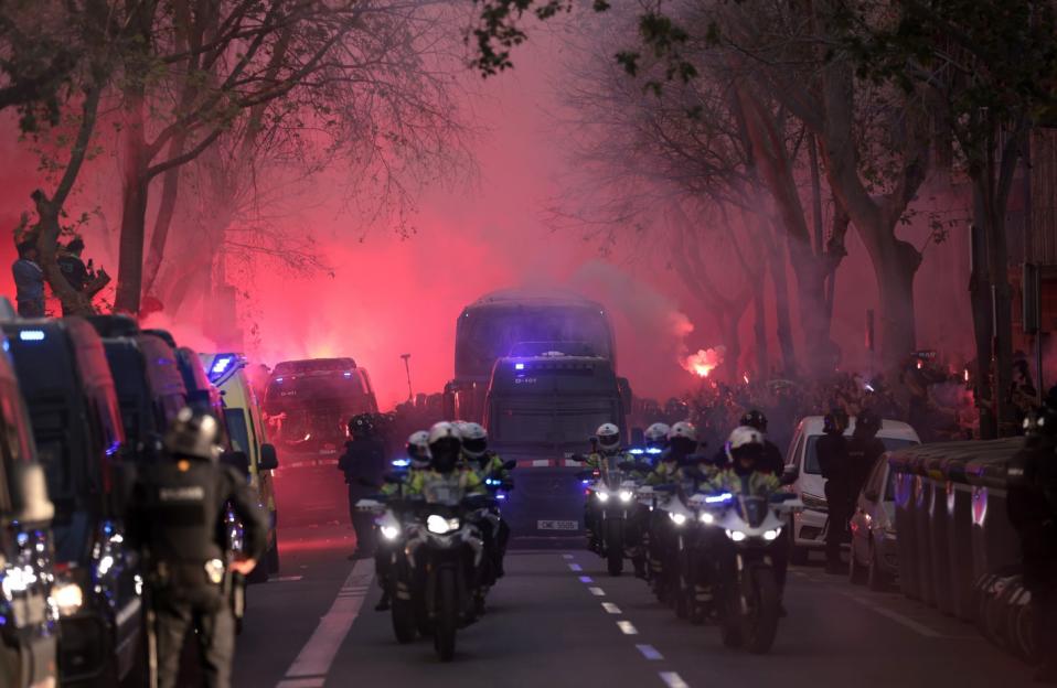 Red smoke from flares surrounds law enforcement vehicles and motorcyclists in a street.