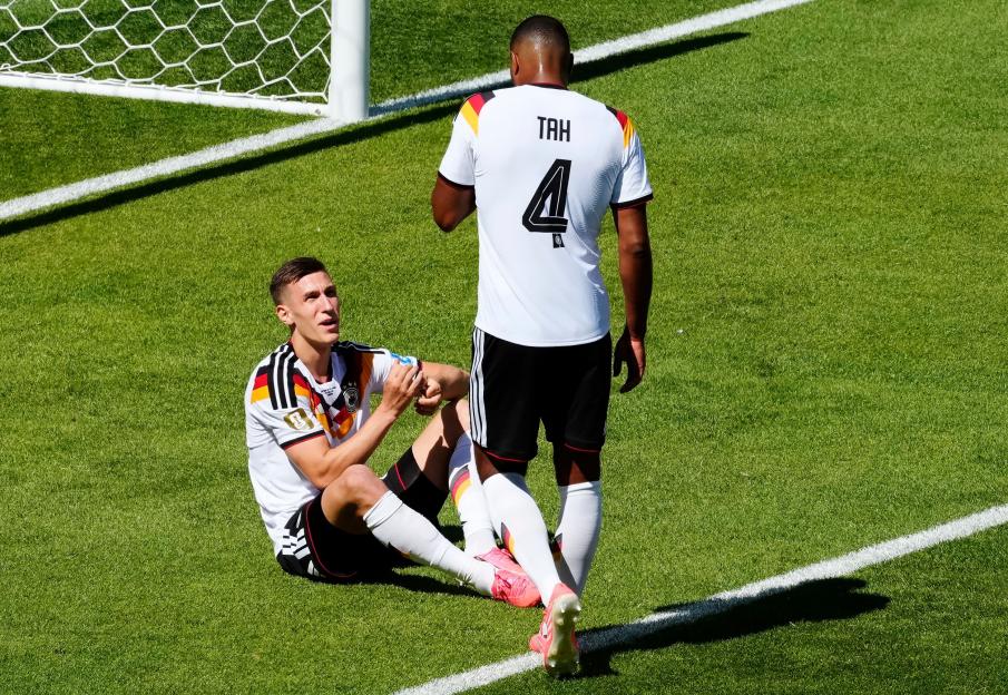 Two German soccer players on the field, one sitting and one standing, during a World Cup match.