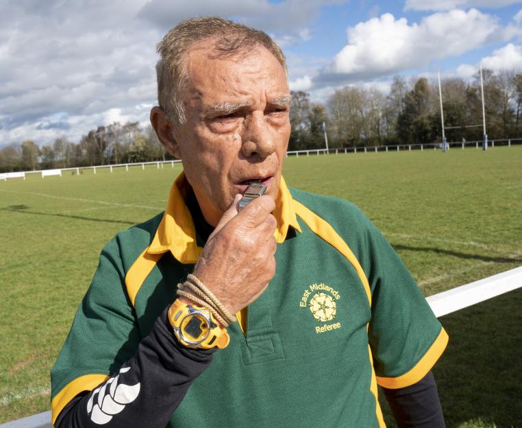 Britain's oldest rugby referee, Nando Di Matteo, 87, blows a whistle on the field.
