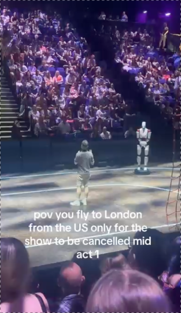A theater performer on stage with a robot mannequin as the audience watches from their seats.