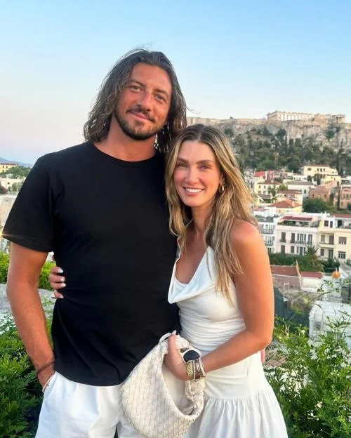 Delta Goodrem and her husband Matthew standing outdoors with a city view in the background.