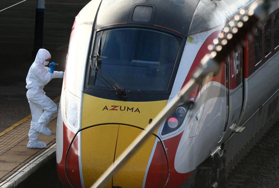 A forensic officer in a white protective suit and blue gloves inspects the front of a London North Eastern Railway (LNER) train on a platform.