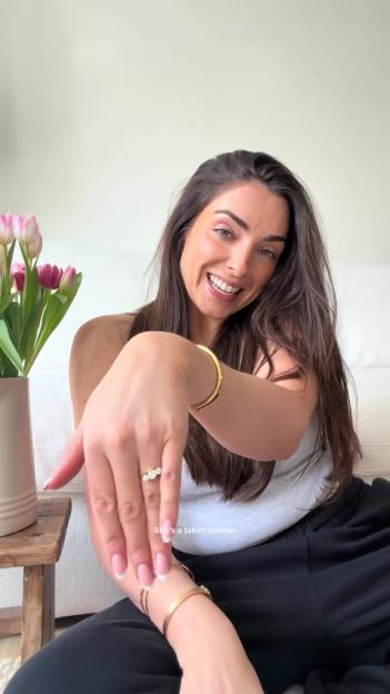 A smiling woman showing off a diamond ring on her left ring finger.