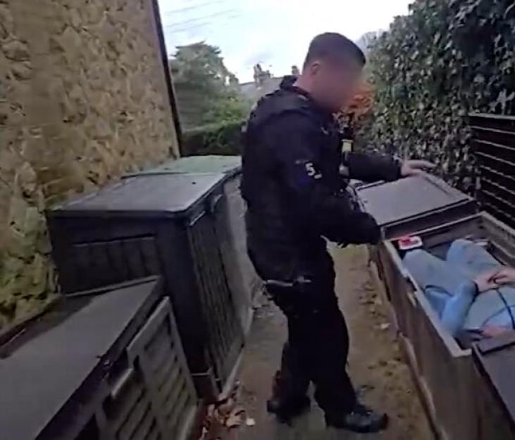 A police officer apprehends a man found hiding in a garden box.