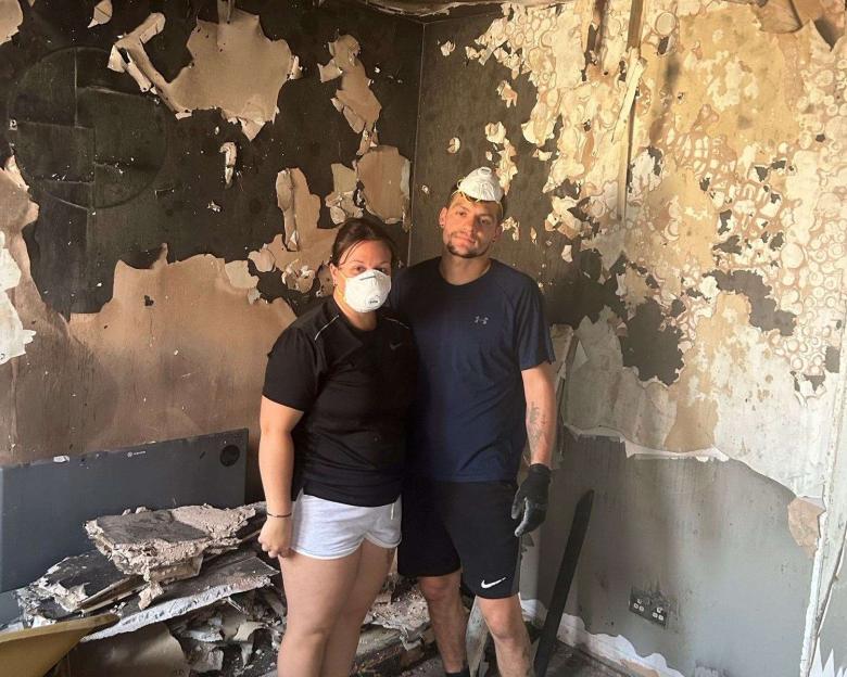 A couple in face masks stand in their fire-damaged home.