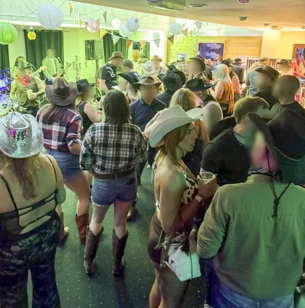 A crowd of people in cowboy hats and western wear socialize at an evening event with green and yellow lighting.
