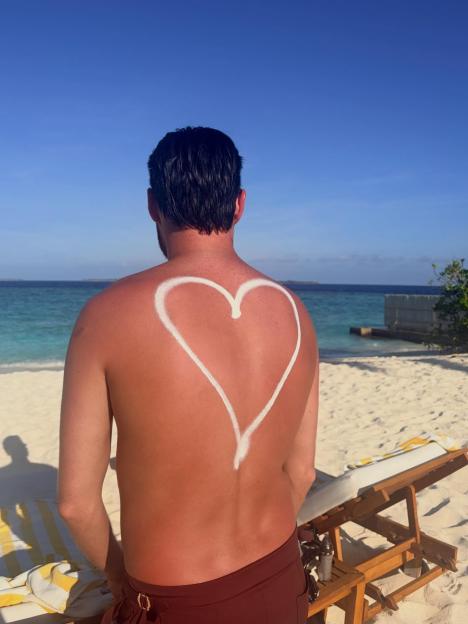 A person with a heart drawn on their back with sunscreen standing on a beach.