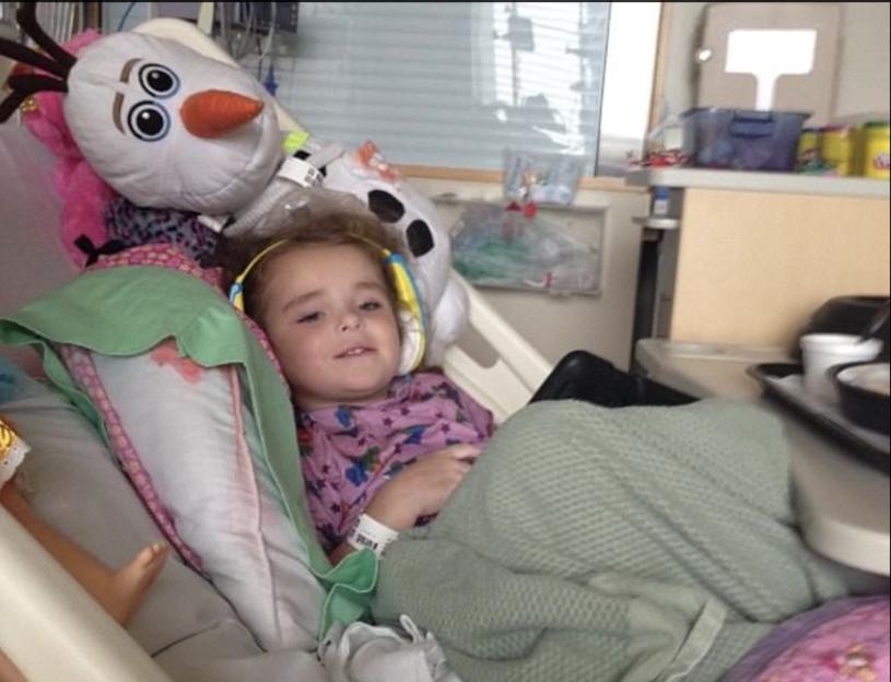 Olivia Gant lying in a hospital bed with a plush Olaf toy beside her.