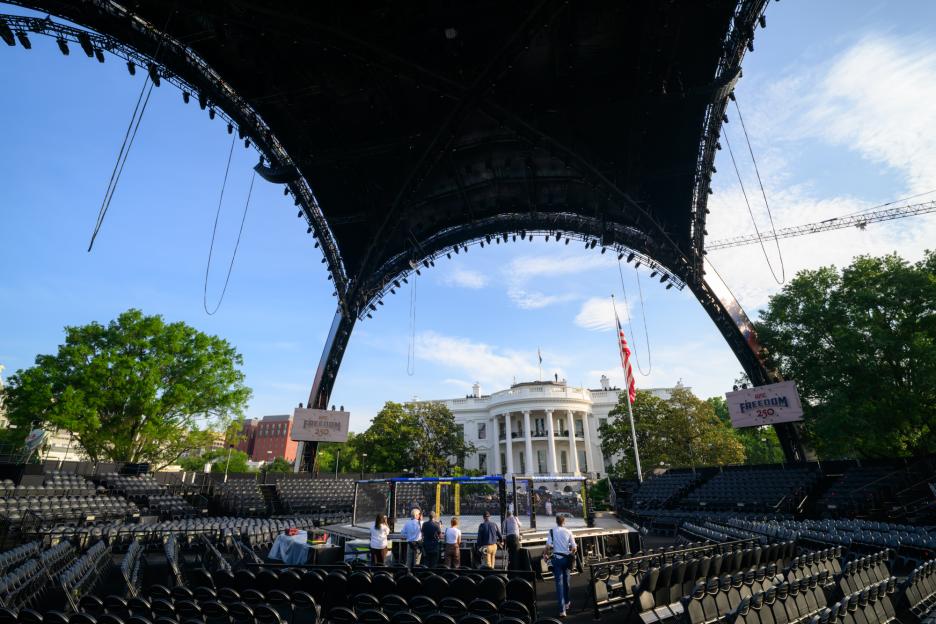 An outdoor event space with empty seats and an octagon fighting ring, with the White House visible in the background under a large black canopy.