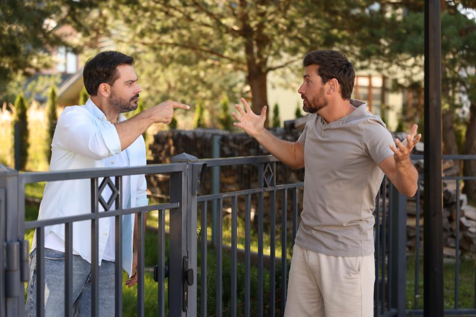 Two adult men arguing over a fence in a neighborhood.
