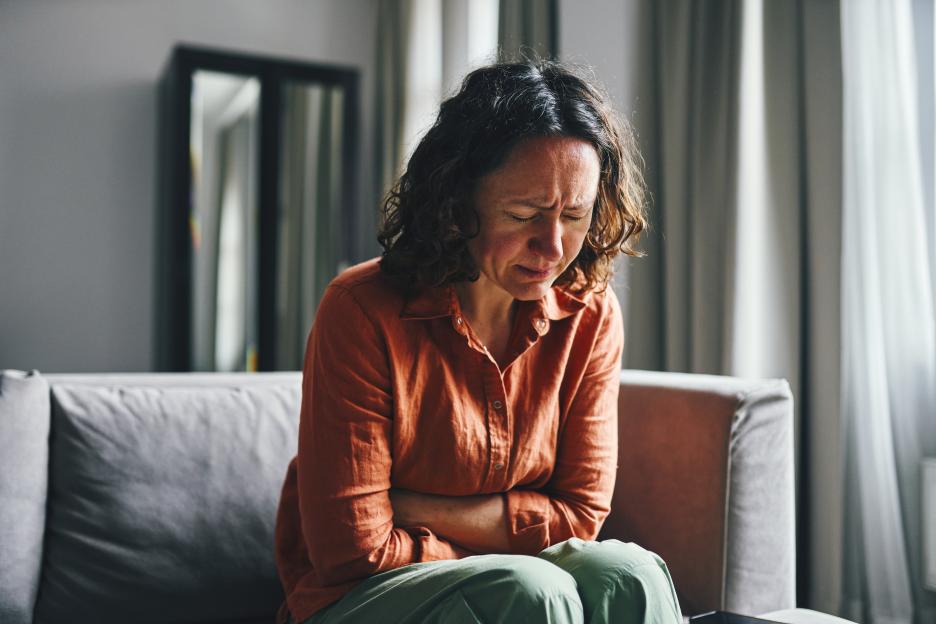Woman sitting on a couch experiencing severe abdominal pain.