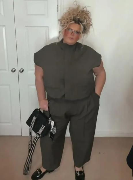 A woman wearing a size 22 F&F co-ord outfit in olive green, with a black handbag, stands in front of a white door.