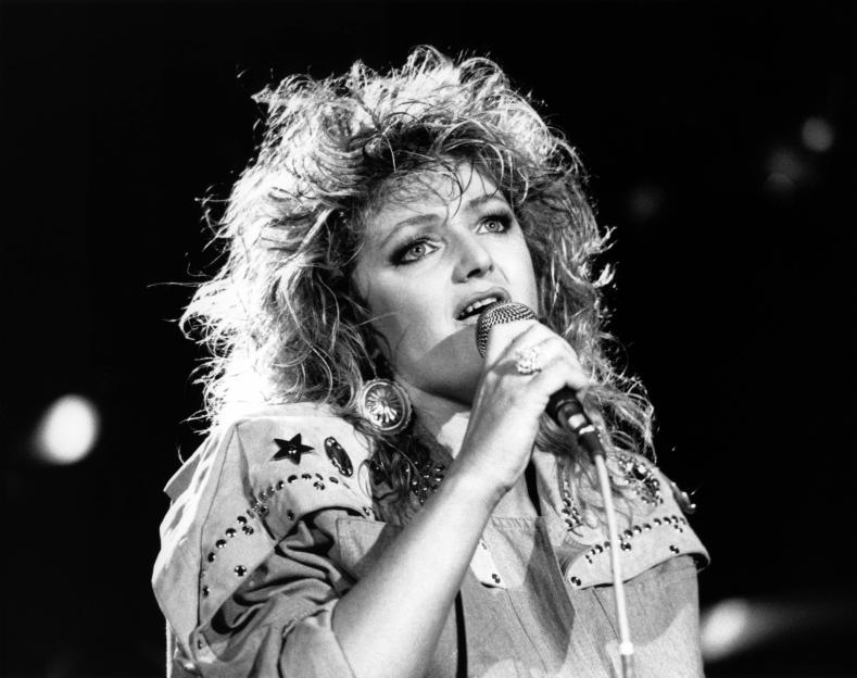 Black and white photo of Bonnie Tyler singing into a microphone.