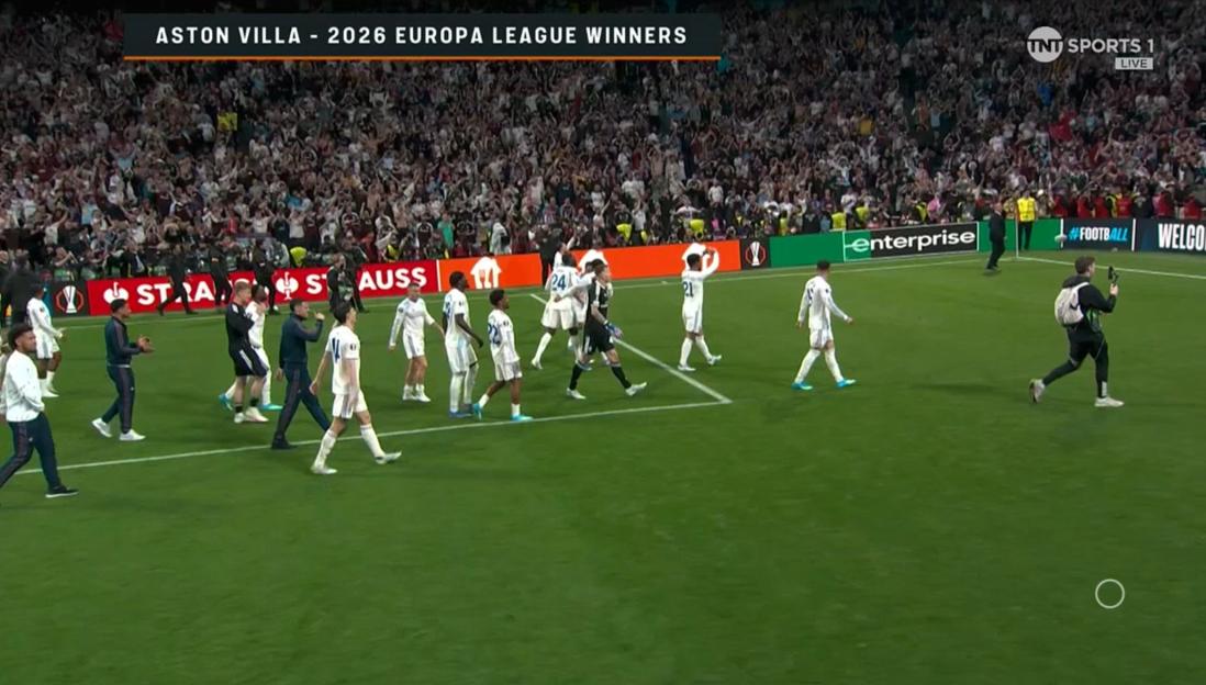 A crowd cheers in a soccer stadium as Aston Villa players walk off the field after winning the 2026 Europa League.