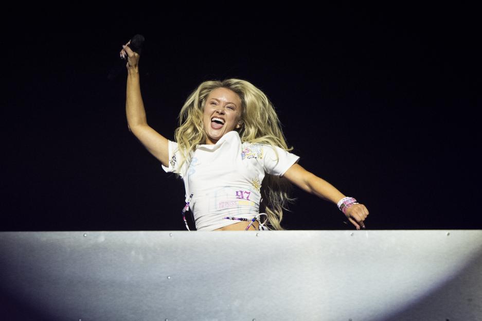 Singer Zara Larsson performs on stage with her arm raised, holding a microphone.