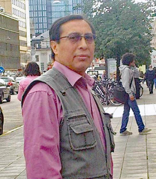 Fredi Rivero, wearing a pink shirt and dark vest, looking at the camera with a city street in the background.
