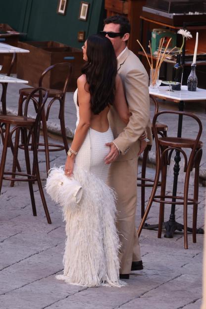 Dua Lipa in a white feathered dress with Callum Turner in a tan suit, his hand on her lower back.
