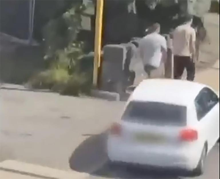 A white car driving toward two men walking away from a street fight.