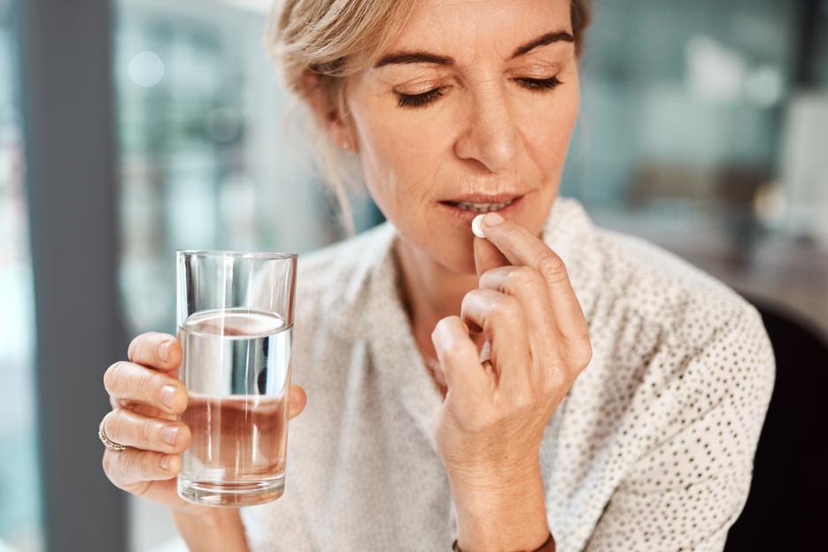 A mature businesswoman takes a pill while holding a glass of water.